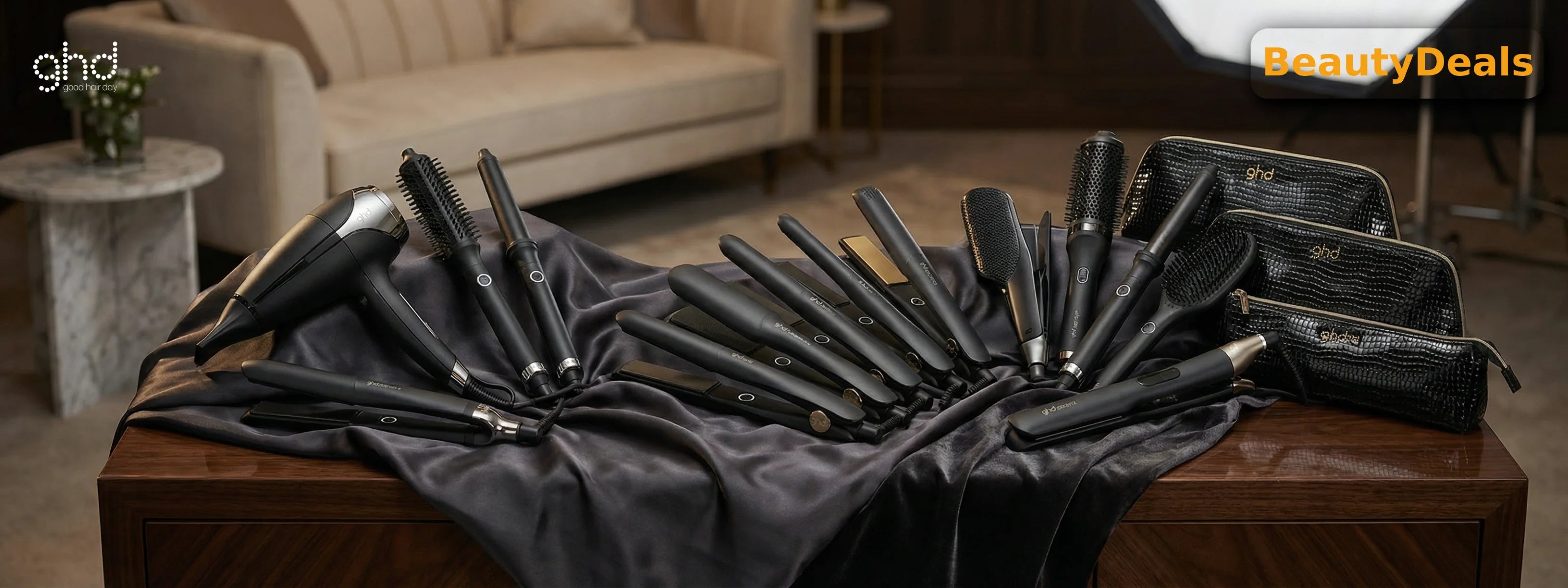 A wide array of black ghd professional hair styling tools, including blow dryers, flat irons, curling wands, and brushes, displayed on a dark silk cloth.
