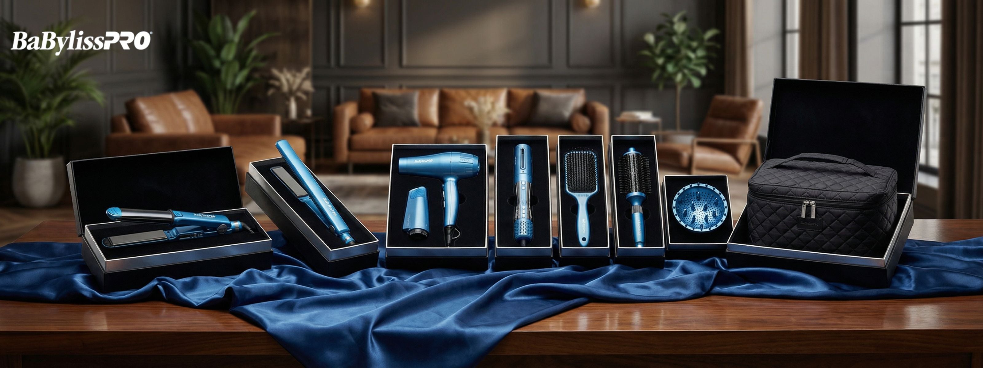 A panoramic display of BaBylissPRO hair styling tools in a shimmering metallic blue finish. The set includes a flat iron, blow dryer, curling wand, and styling brushes, each presented in luxury black gift boxes on a wooden table draped with blue silk.